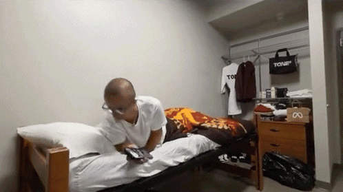 A Man Is Laying On A Bed In A Room With A Bag That Says Tour GIF
