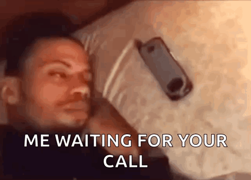 A Man Is Laying On A Bed With A Cell Phone In His Hand And The Words " Me Waiting For Your Call " Above Him GIF
