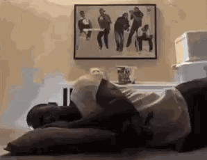 A Man Is Laying On A Bed With A Pillow And A Picture On The Wall Behind Him . GIF