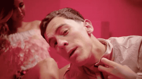 A Man Is Laying On A Bed With A Woman In A Pink Dress Behind Him GIF