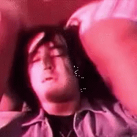 A Man Is Laying On A Bed With His Eyes Closed And A Woman Is Holding His Head . GIF
