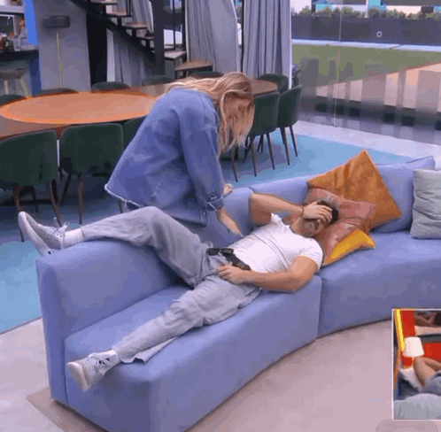 A Man Is Laying On A Blue Couch While A Woman Touches His Forehead GIF