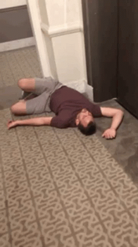 A Man Is Laying On A Carpet In A Hallway . GIF