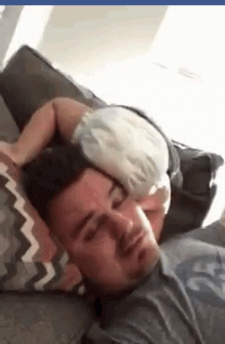 A Man Is Laying On A Couch With A Baby Sleeping On His Head . GIF