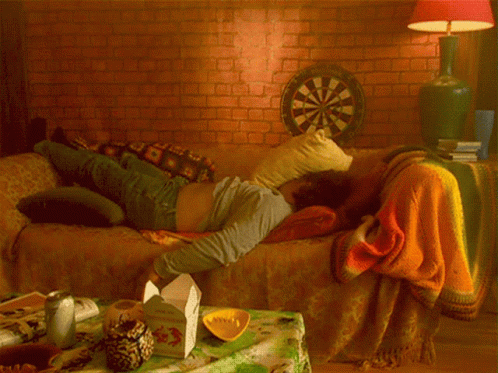 A Man Is Laying On A Couch With A Dart Board In The Background GIF