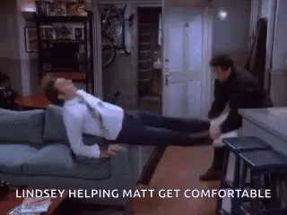 A Man Is Laying On A Couch With A Woman Standing Next To Him And The Words Lindsey Helping Matt Get Comfortable Above Hi GIF