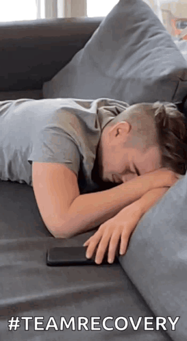 A Man Is Laying On A Couch With His Head On His Hands And A Cell Phone . GIF
