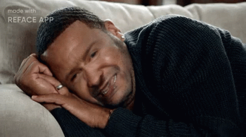 A Man Is Laying On A Couch With His Head On His Hands . GIF