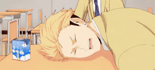 A Man Is Laying On A Desk In A Classroom Next To A Box Of Milk . GIF
