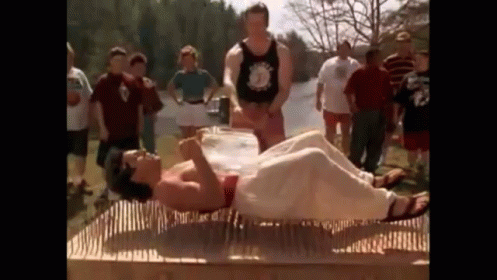 A Man Is Laying On A Mattress Made Of Nails While A Group Of People Watch . GIF