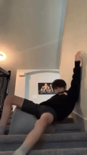 A Man Is Laying On A Staircase With His Legs Crossed And A Picture Of A Man On The Wall Behind Him . GIF