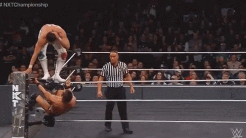 A Man Is Laying On His Back In A Wrestling Ring While Another Man Kicks Him . GIF