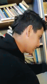 A Man Is Laying On His Back In Front Of A Bookshelf Filled With Books . GIF