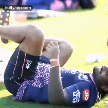a man is laying on his stomach on the grass and stretching his leg .