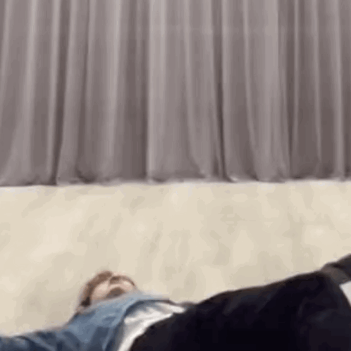 A Man Is Laying On The Floor In Front Of A Curtain In A Room . GIF