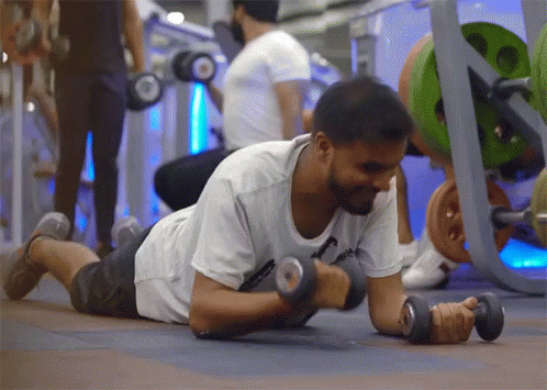 A Man Is Laying On The Floor Lifting Dumbbells GIF