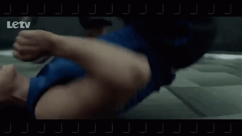 A Man Is Laying On The Floor While Another Man Is Running In A Hallway . GIF