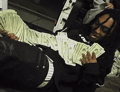A Man Is Laying On The Ground Holding A Stack Of 20 Dollars GIF