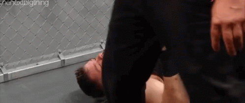 A Man Is Laying On The Ground In A Boxing Ring While Another Man Is Standing Over Him . GIF