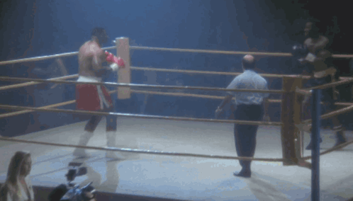 A Man Is Laying On The Ground In A Boxing Ring While Another Man Watches GIF