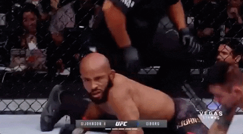 A Man Is Laying On The Ground In A Cage During A Boxing Match . GIF