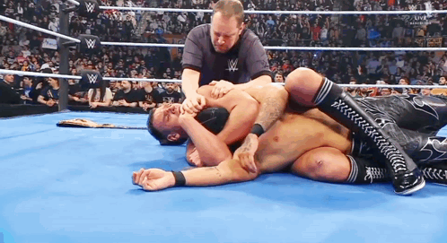 A Man Is Laying On The Ground In A Wrestling Ring While A Referee Watches . GIF