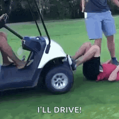 A Man Is Laying On The Ground Next To A Golf Cart While Another Man Stands Behind Him . GIF