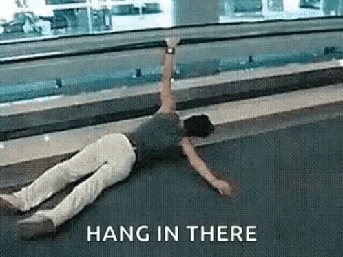 A Man Is Laying On The Ground With The Words Hang In There Above Him . GIF