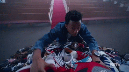 A Man Is Laying On Top Of A Pile Of Shoes With A Bet Logo In The Background GIF