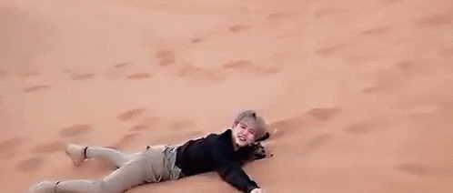 A Man Is Laying On Top Of A Sand Dune In The Desert . GIF