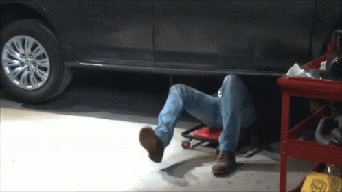 A Man Is Laying Under A Car In A Garage With His Head Underneath The Car GIF