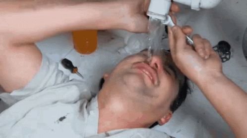 A Man Is Laying Under A Sink With Water Coming Out Of The Pipes GIF