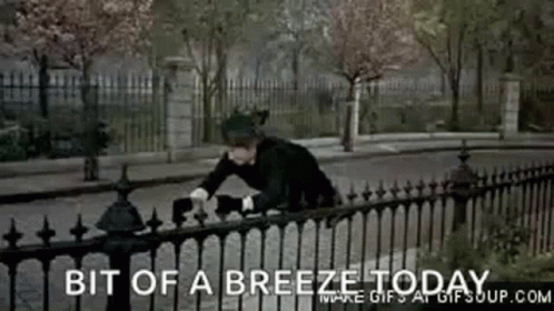 A Man Is Leaning Over A Fence With The Words Bit Of A Breeze Today Written Below Him GIF