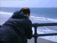 Man Leaning Over Railing Looking At Ocean GIF