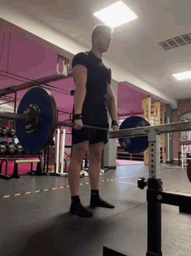 A Man Is Lifting A Barbell In A Gym With A Pink Wall Behind Him GIF