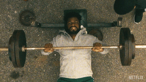 A Man Is Lifting A Barbell On A Bench With Netflix Written On The Bottom GIF