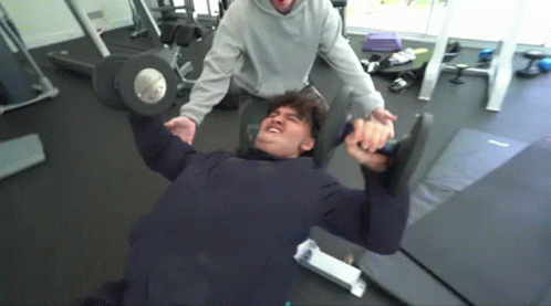 A Man Is Lifting A Dumbbell In A Gym . GIF