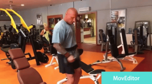 A Man Is Lifting A Dumbbell In A Gym With A Moveeditor Watermark GIF