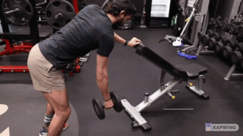 A Man Is Lifting A Dumbbell On A Bench In A Gym With A Caption That Says Kapwing GIF
