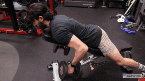 A Man Is Lifting A Dumbbell On A Bench In A Gym With Kapwing Written In The Corner GIF