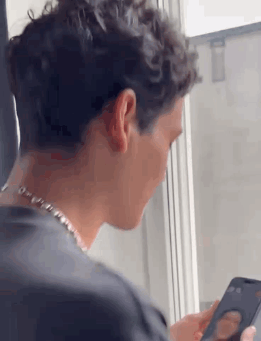 a man is looking at a cell phone while sitting in front of a window .