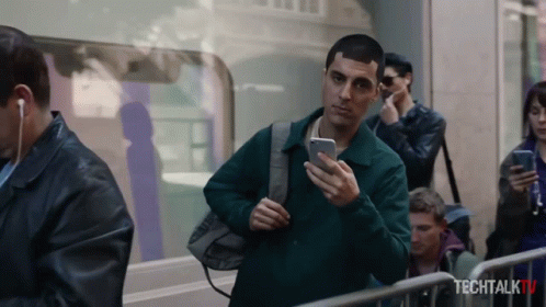 A Man Is Looking At His Phone In Front Of A Sign That Says Tech Talk Tv GIF