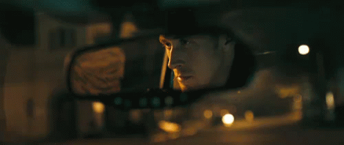 A Man Is Looking At His Reflection In The Rear View Mirror Of A Car . GIF