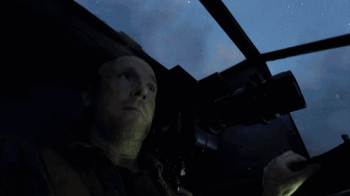 A Man Is Looking Out A Window With A Blue Light Behind Him GIF
