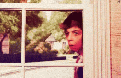 A Man Is Looking Out Of A Window And Making A Funny Face . GIF