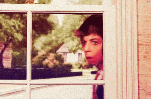 A Man Is Looking Out Of A Window And Making A Funny Face . GIF