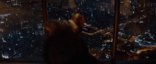 A Man Is Looking Out Of A Window At A City GIF