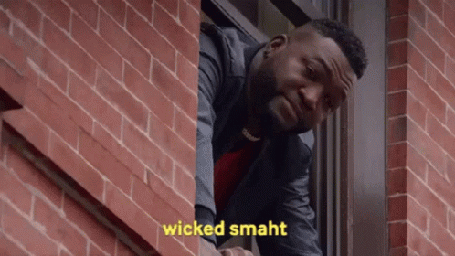 a man is looking out of a window with the words wicked smaht written on the brick wall behind him .