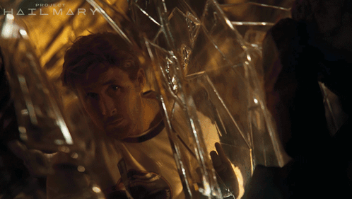 A Man Is Looking Through A Broken Glass Window With The Words Project Hailmary Behind Him GIF