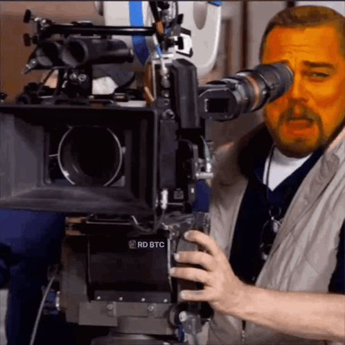 A Man Is Looking Through A Camera With Rd Btc Written On It GIF